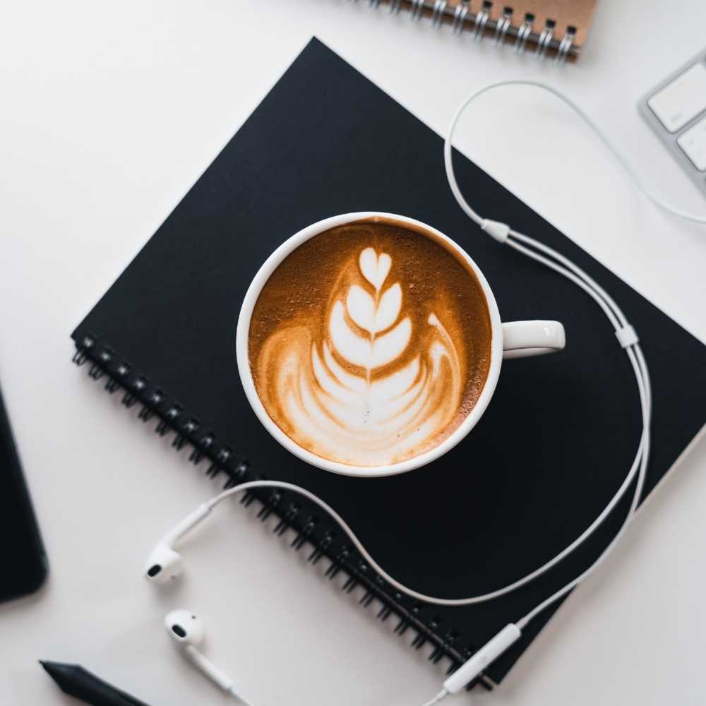 Personal Brand Coach Coffee cup journal and ear pods on desk